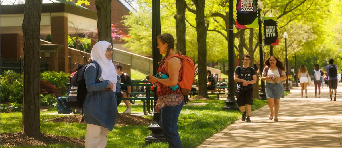 Two young women talk on a campus sidewalk