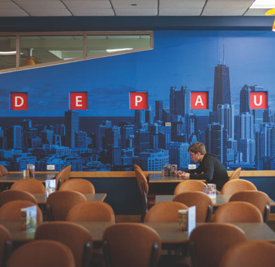 A young man sits alone in a dining area with a DePaul mural